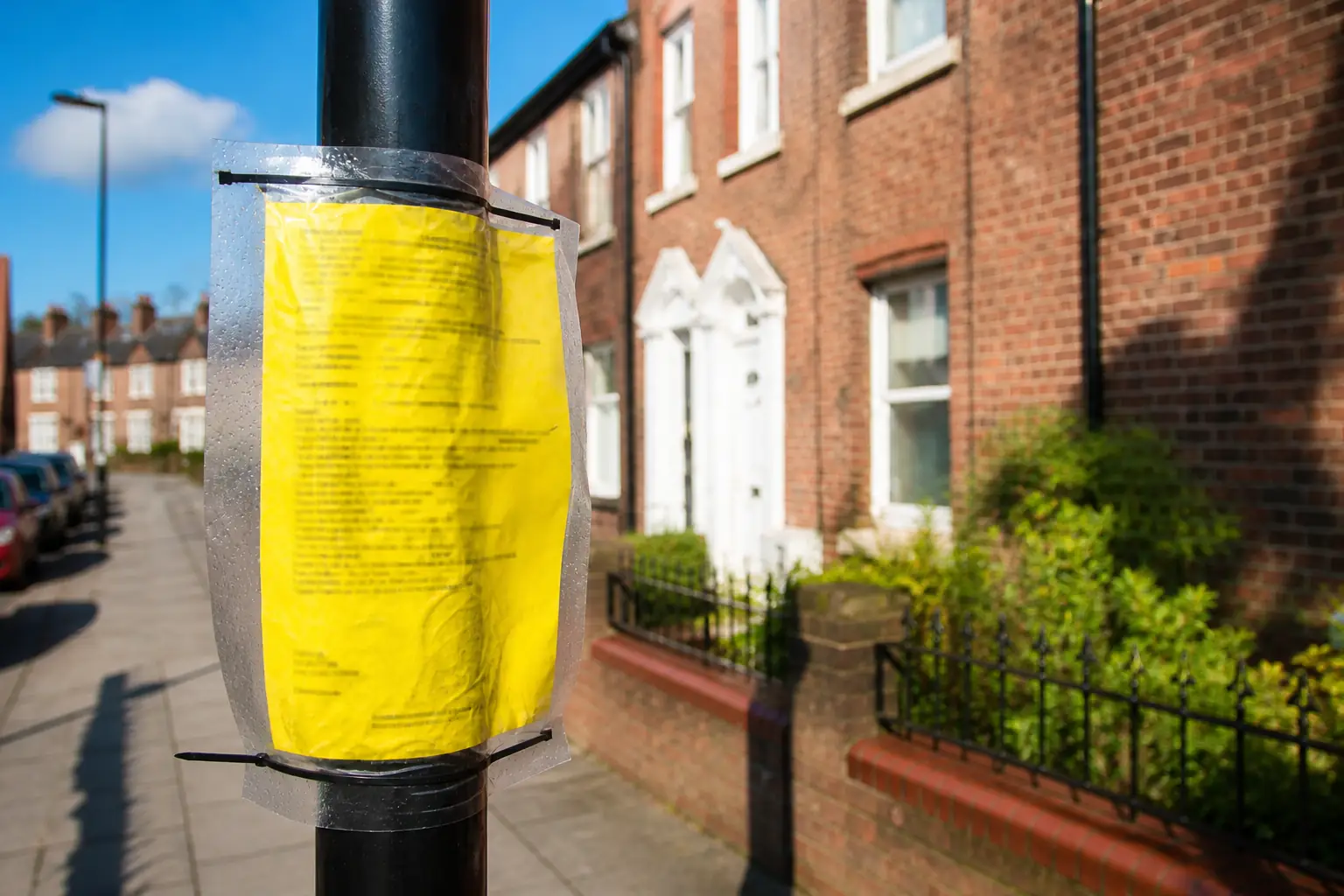 A yellow planning notice in a plastic sleeve on a lamp post